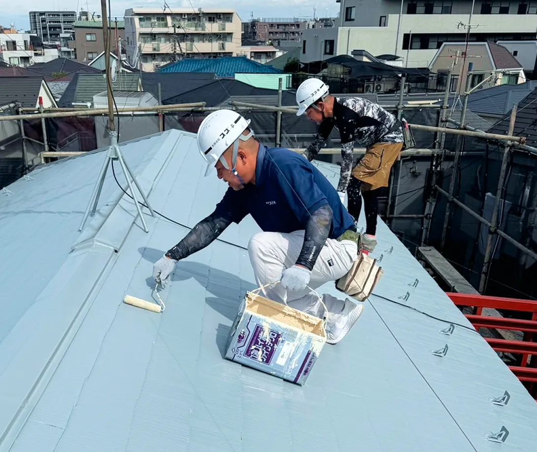 都会の屋根の上で、丁寧に塗料を塗る作業。職人たちの集中力と技術が光る瞬間。